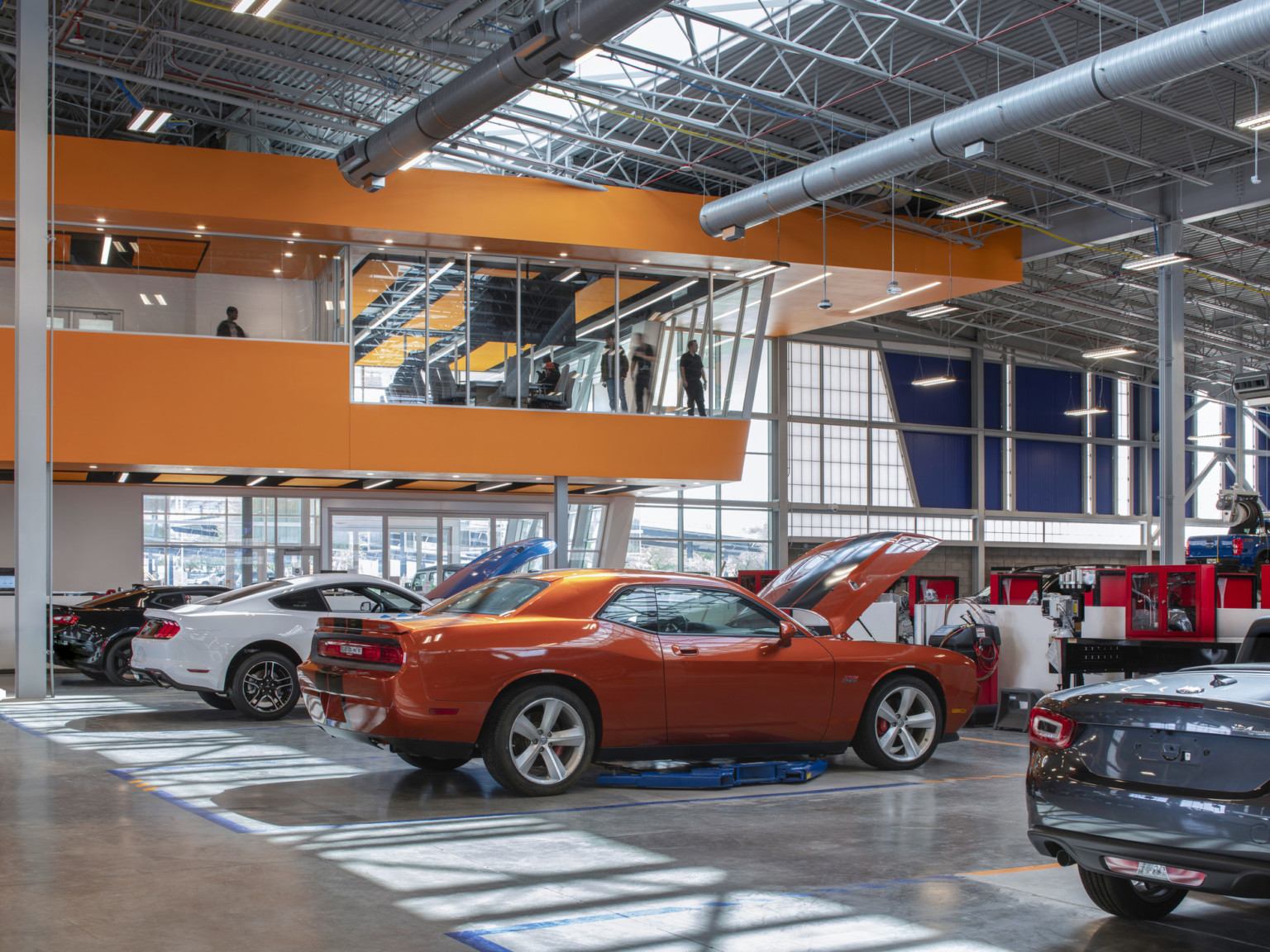 Glass room with Orange car under glass bannister to exposed second floor. Orange detail left