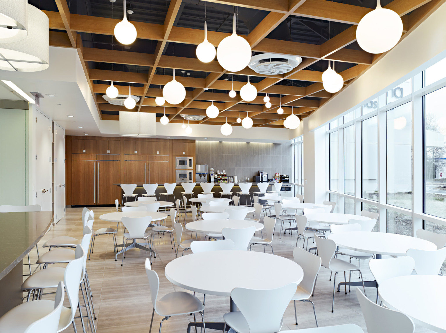 dining area with white circle tables, warm wood walls, and lit up globe pendants hanging from the ceiling