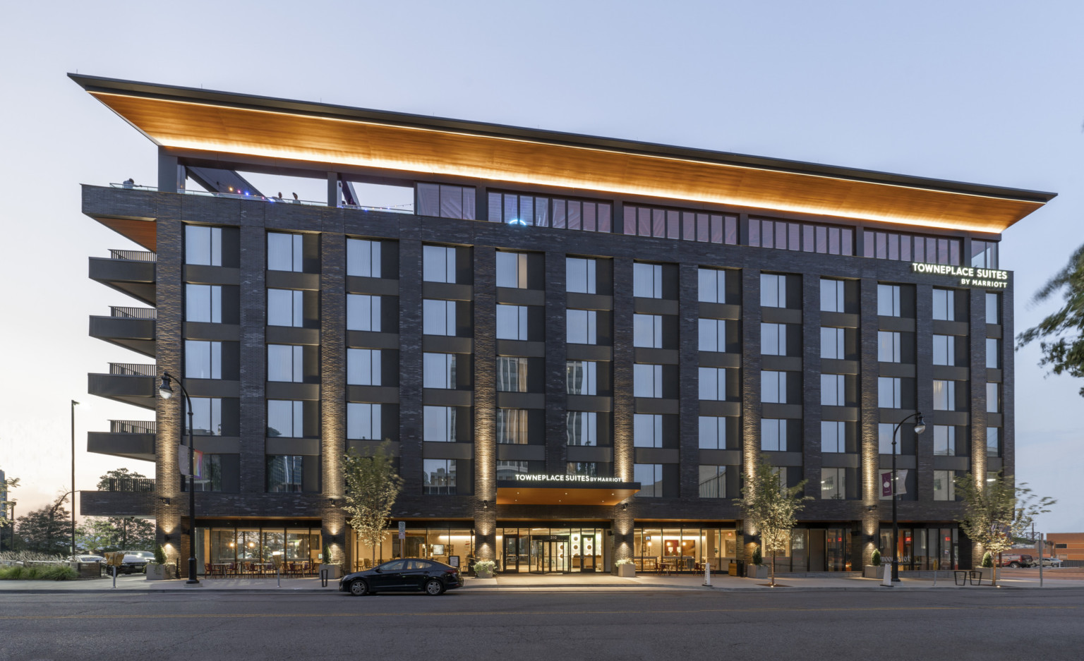 The Towneplace Suites Nashville Downtown seen from street level features assorted tones of gray stone scaling the sides while a warm, honey wood ceiling runs the length of the roof deck.