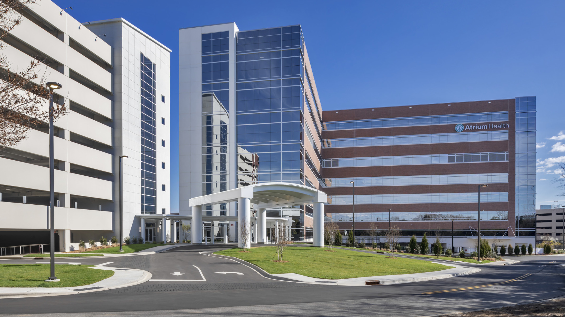 Atrium Health Pineville Bedtower Expansion. A multistory tower with white arching carport over drive. Garage to left