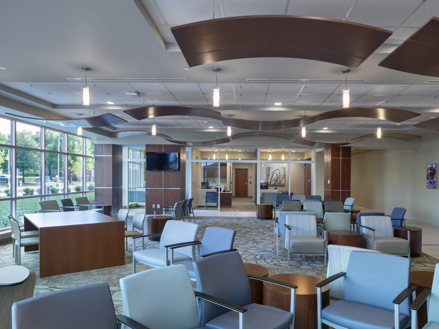 Waiting room lobby with flexible arm chairs and tables. Floor to ceiling windows to left, brown waving acoustic panels hanging