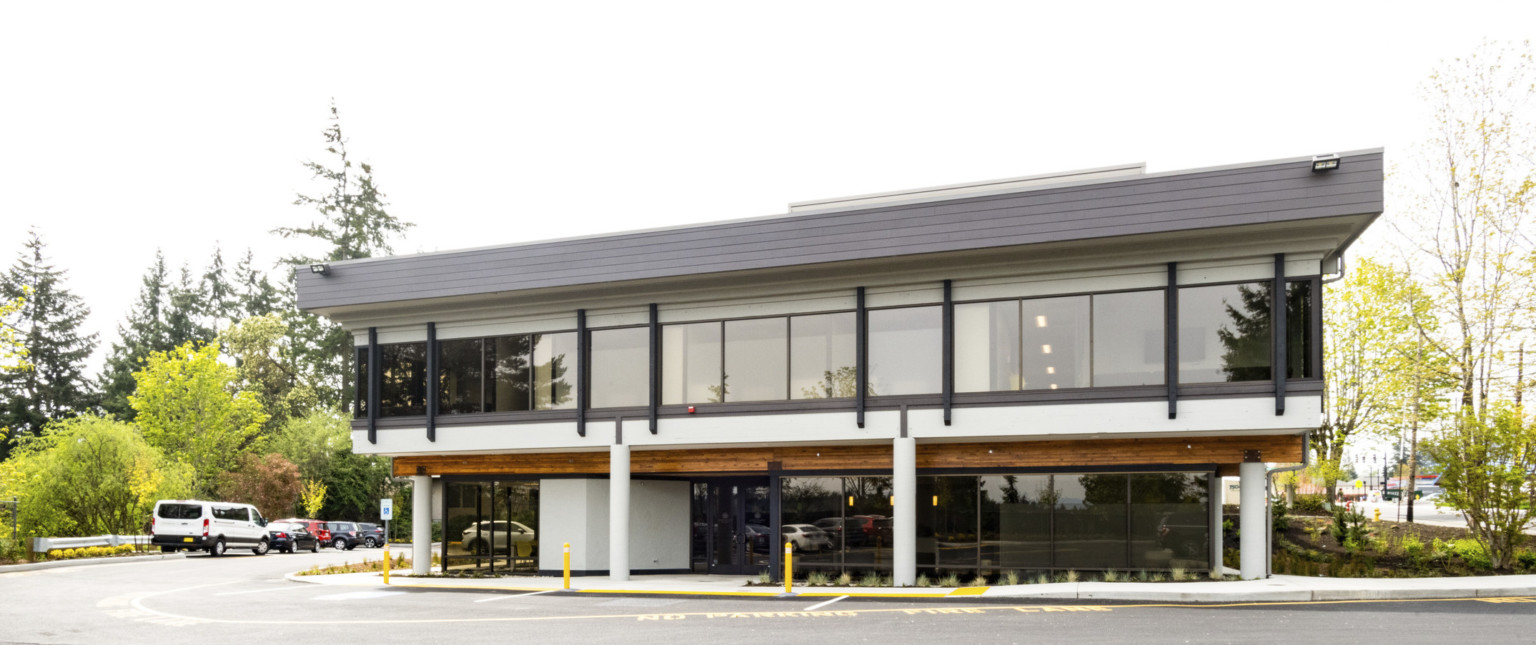 modern building with wooden fascia and white pillars on the first floor, floor to ceiling glass and black fascia on floor 2