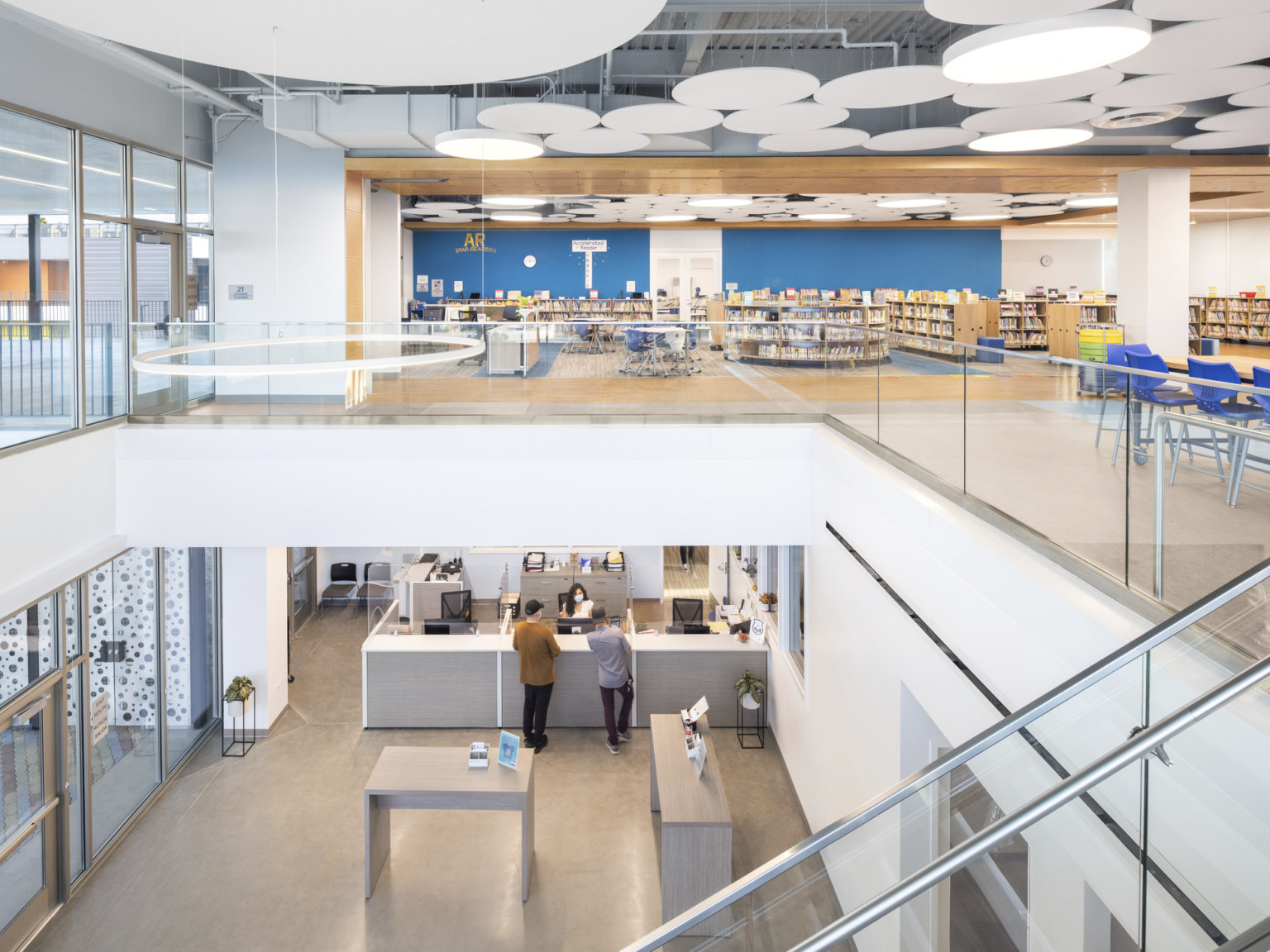 Interior entry with administrative desk in double height atrium. Upper level, bookshelves, mixed flexible seating, ceiling accents