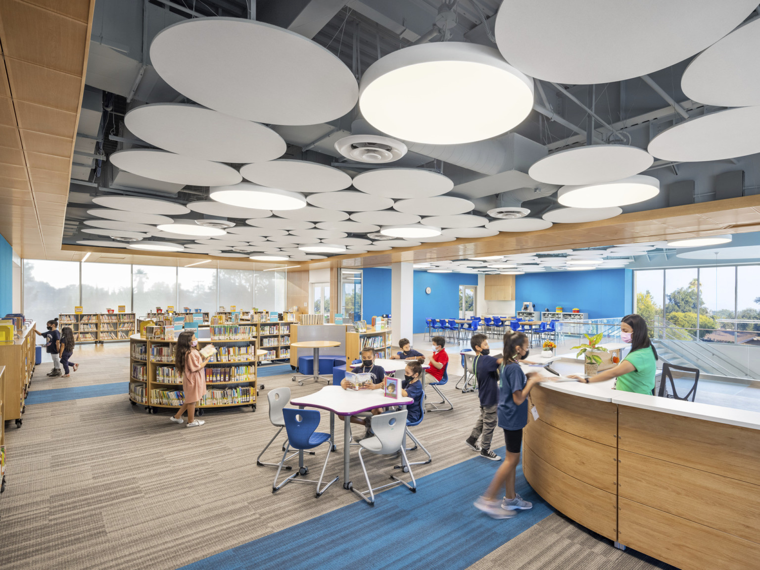 Interior upper level library, mixed flexible seating dispersed among bookshelves. White round accents on ceiling match lights