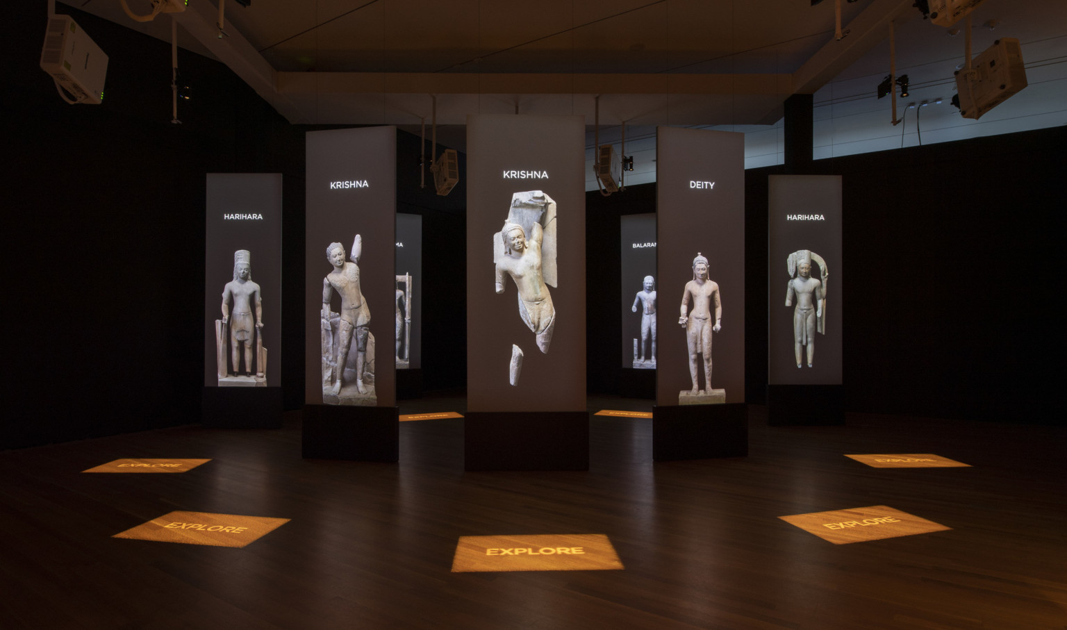 a darkened room with screens and stone statue images suspended in a circle pattern with illuminated signage on the wood floor