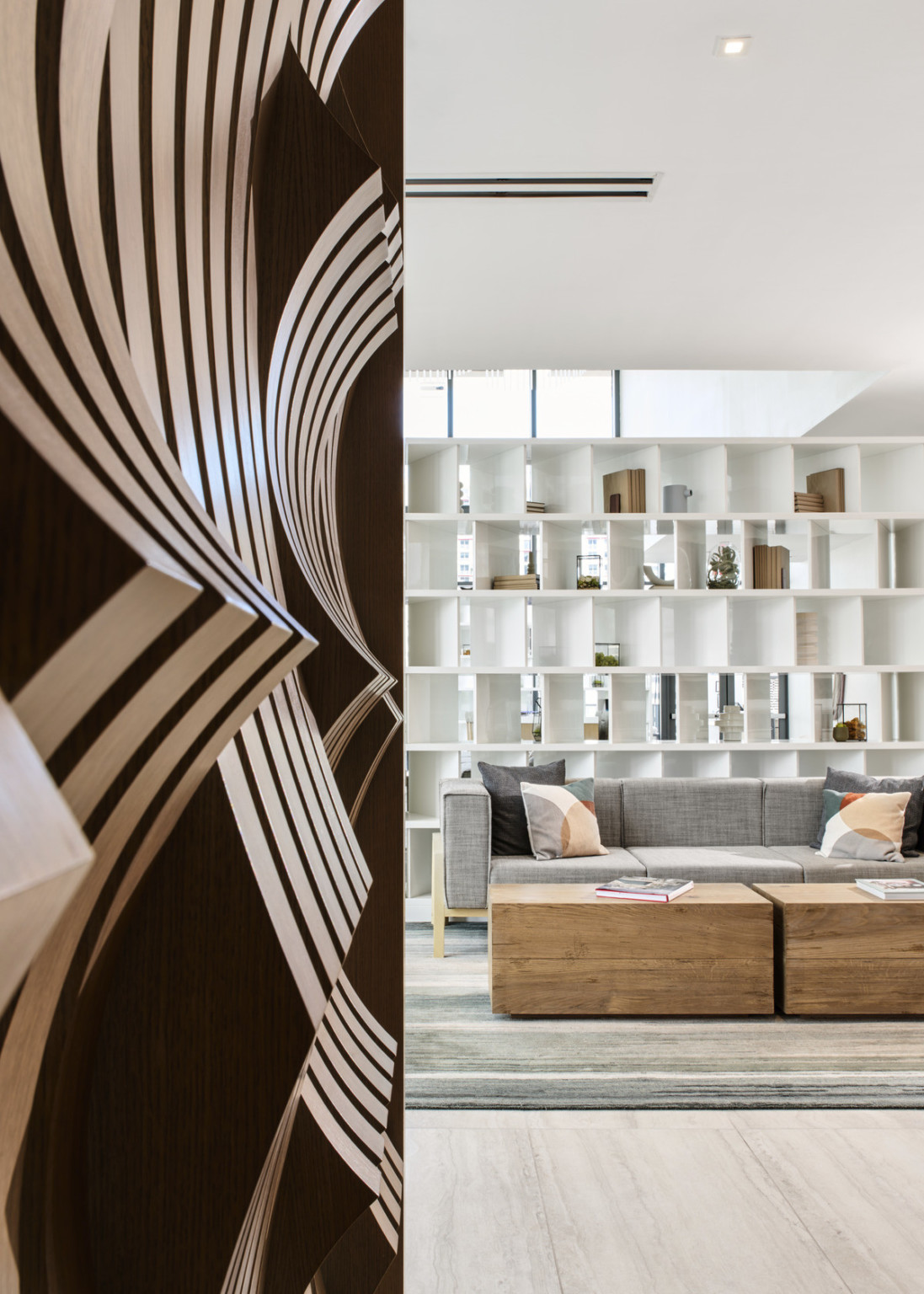 View from reception feature wall to the sun-soaked white and gray palette lounge area with bespoke white shelf room divider