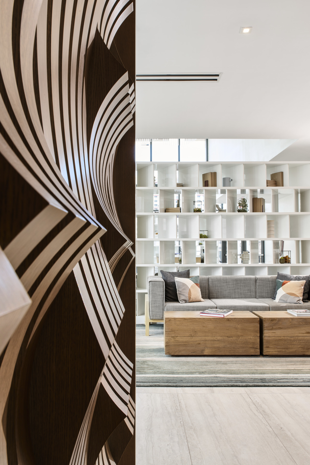View from reception feature wall to the sun-soaked white and gray palette lounge area with bespoke white shelf room divider