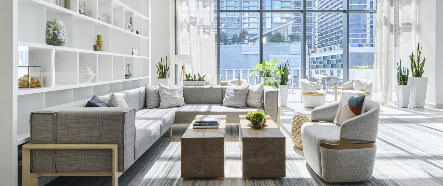 Bespoke white divider shelf in large group with gray, modern seating, wood block coffee table, and planters in double height glass room