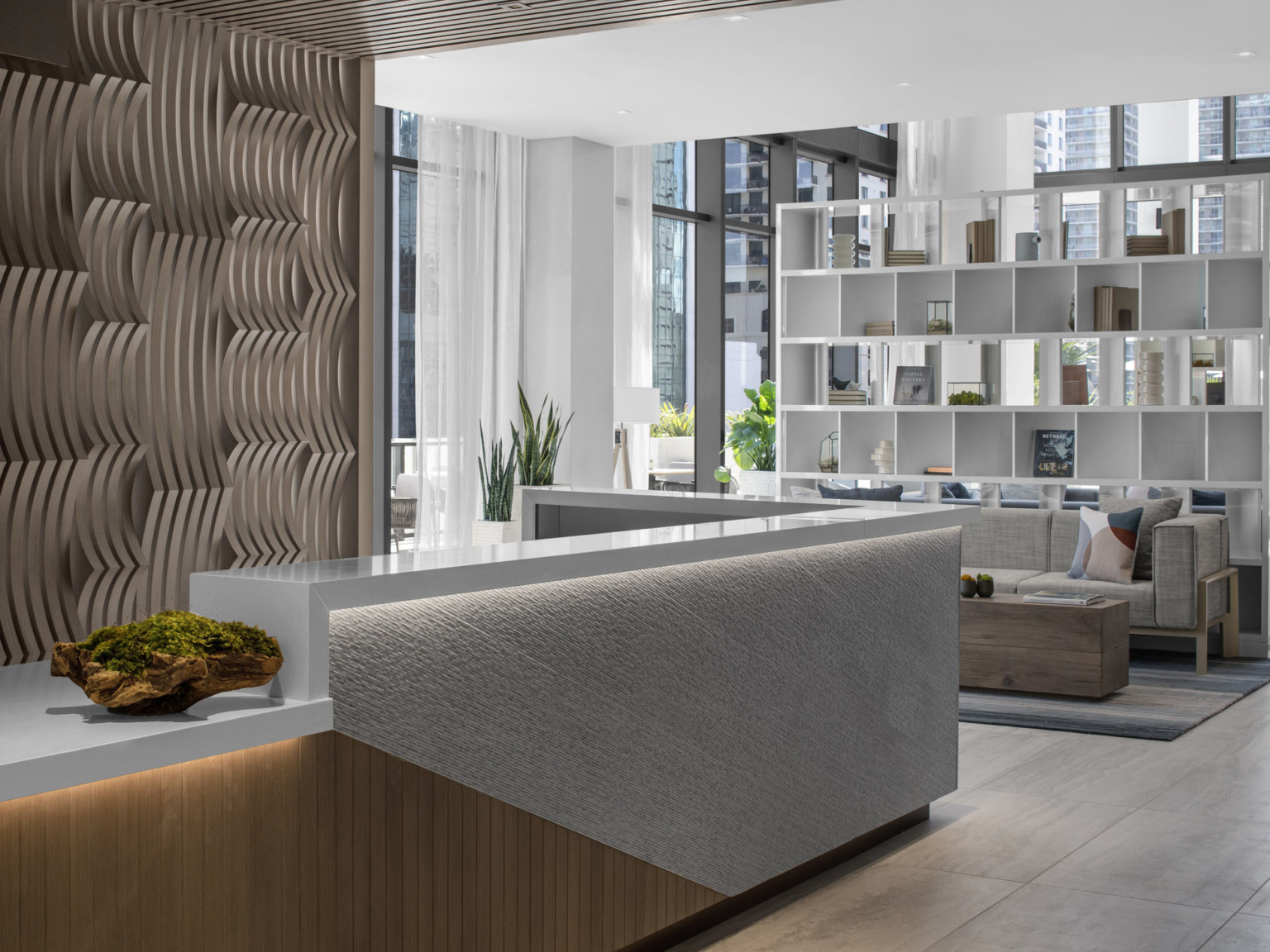 Organically staggered wood pattern backdrop behind a stone and wood reception desk in the Element lobby. White shelf room divider