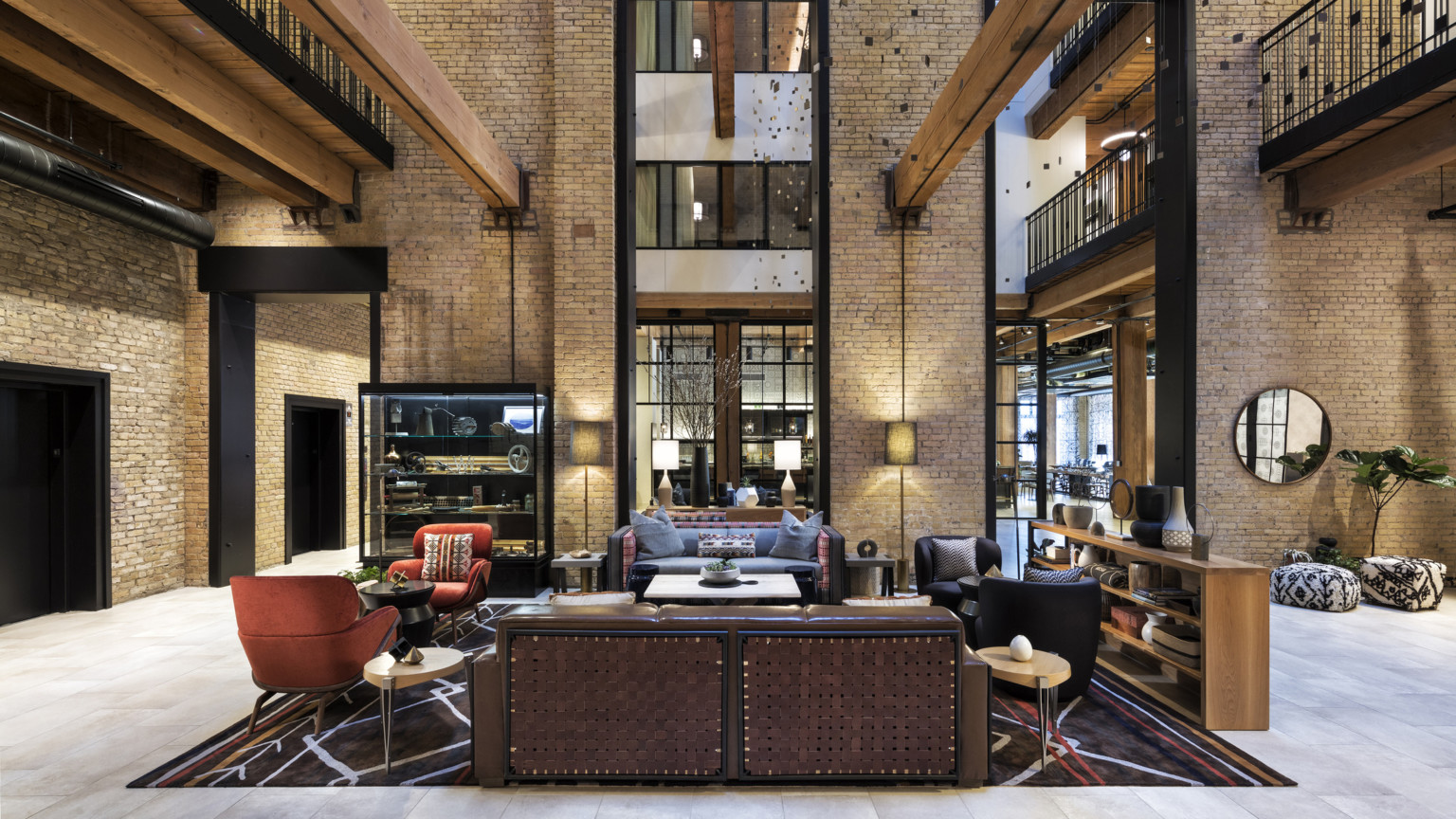 Interior atrium with exposed brick. Seating area at center and wood beams overhead. 2 walkways on sides above with metal rail