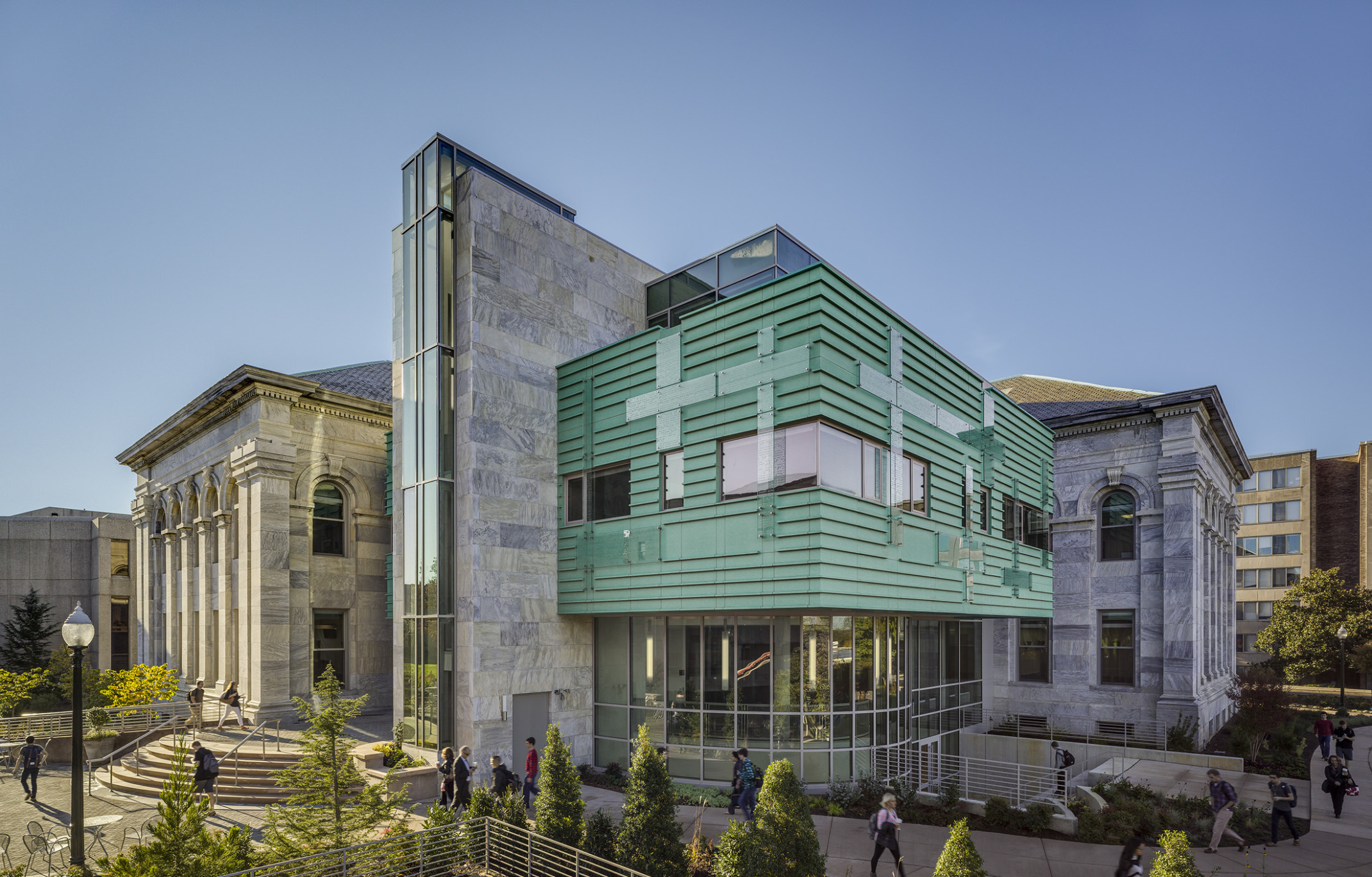 neoclassical stone building with arched windows, columns, radial stairs. modern glass and teal green facade cladding addition