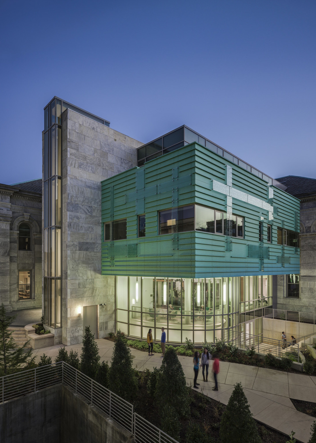 glass building base illuminated against dark sky, modern green facade cladding above, white striated marble volume to the left