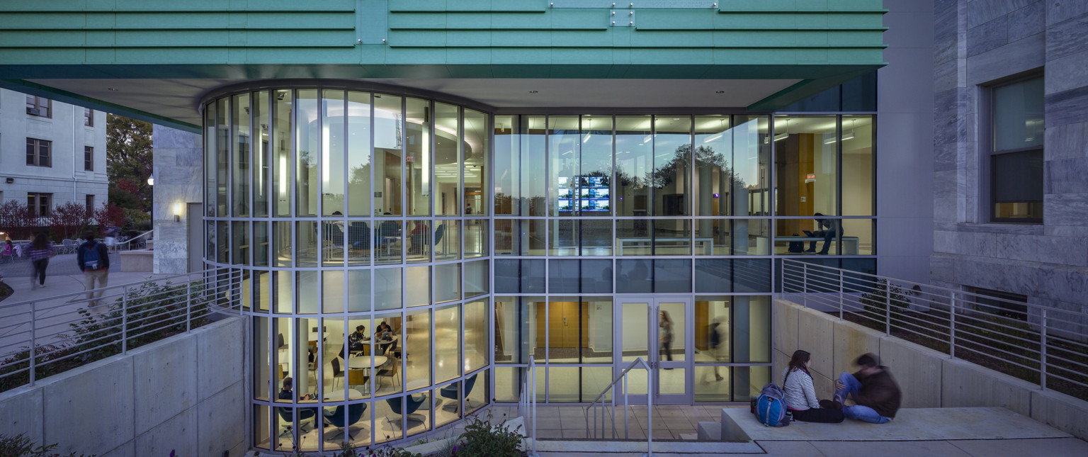 2 story round glass walls and plaza stairs below modern green facade cladding next to gray and white striated marble window