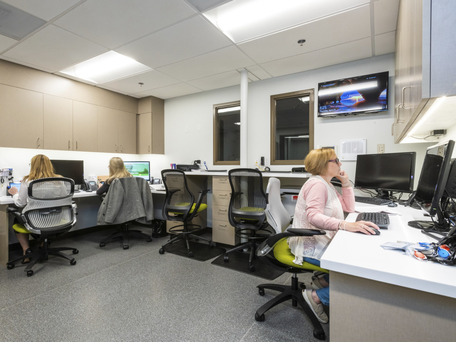 An office space with U-shaped desking individual workstations task chairs hanging cabinet storage and overhead lighting