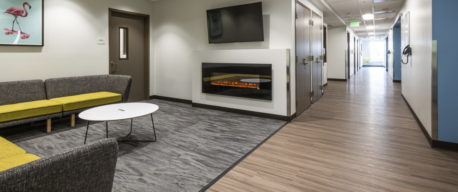 A gray sectional sofa with chartreuse seat cushions in front of a fireplace and TV next to hallway with doors and wood floors