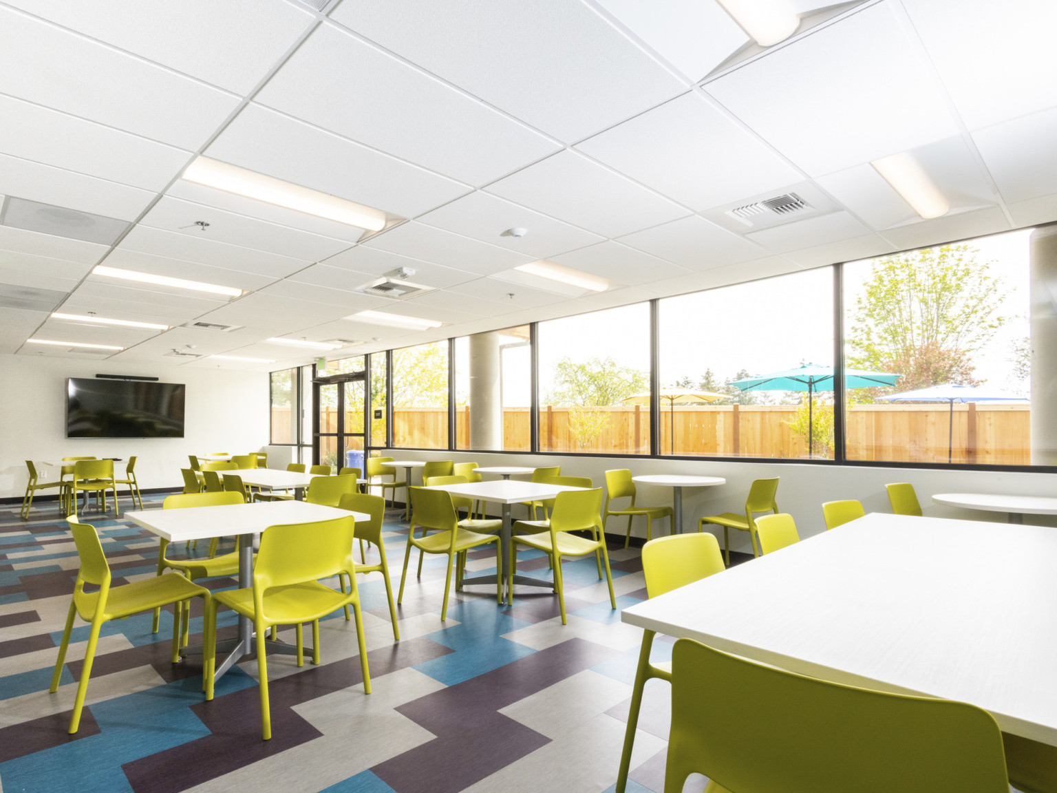 common area with expanse of glass geometric blue purple and tan floors white tables and chartreuse plastic molded chairs