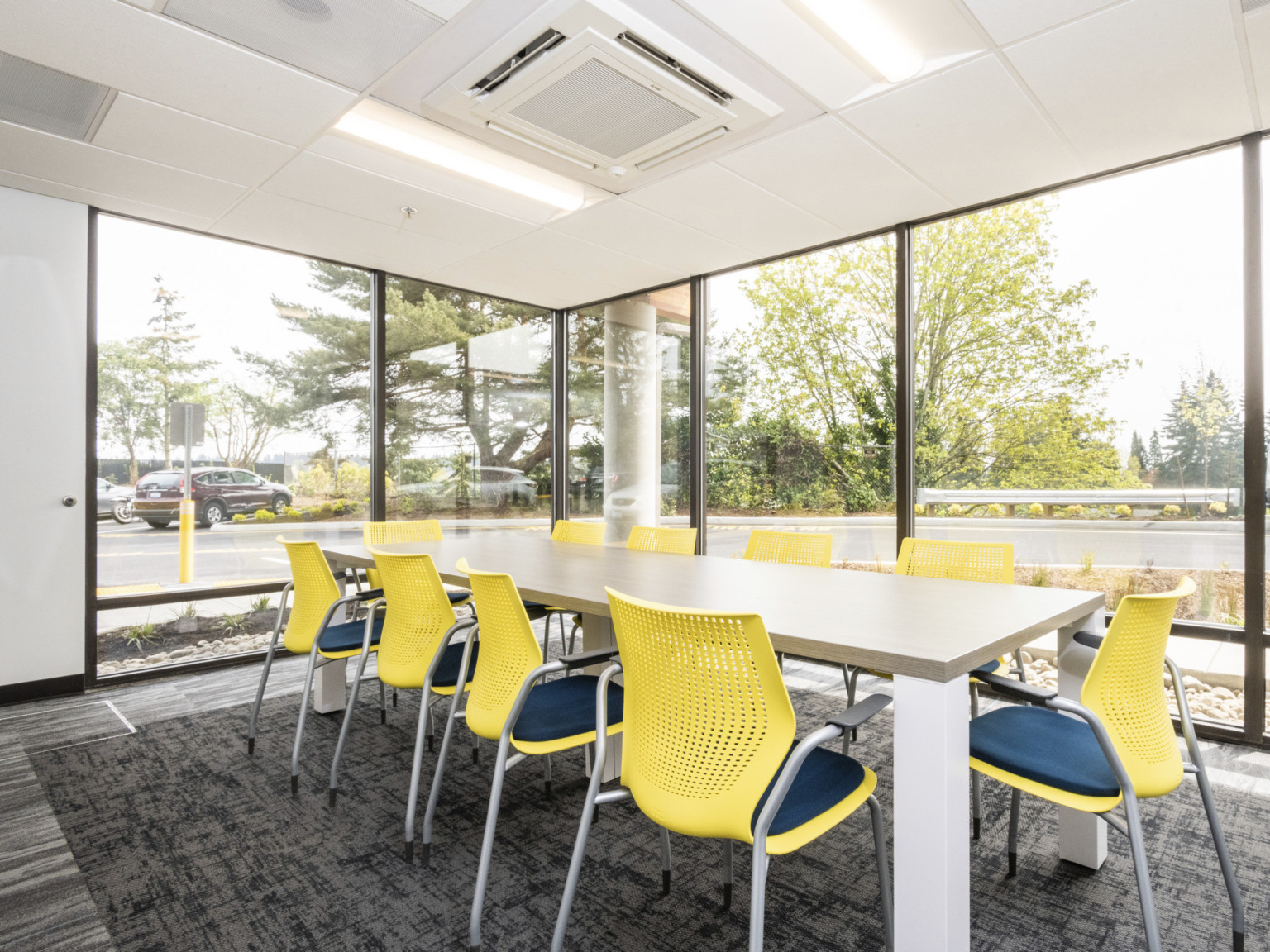 corner conference room with floor to ceiling glass gray carpet gray LVT floors white walls and ceiling and yellow chairs