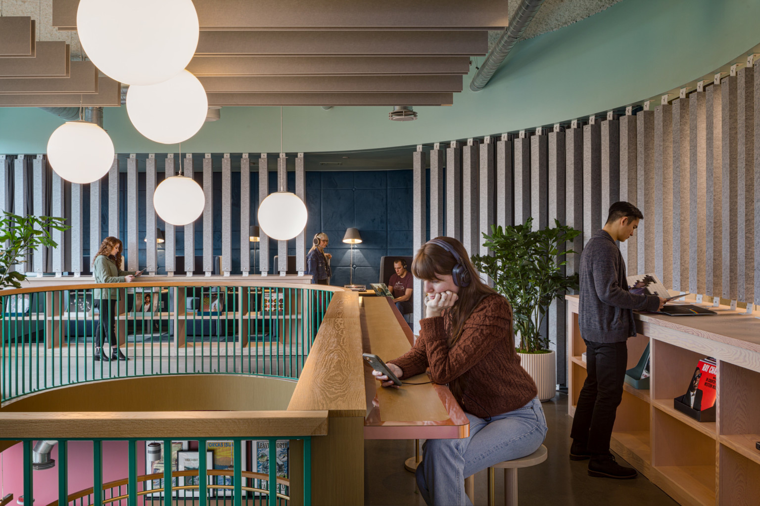 a woman on her phone with headphones sits at a radial wooden counter overlooking a mezzanine finished in wooden slats