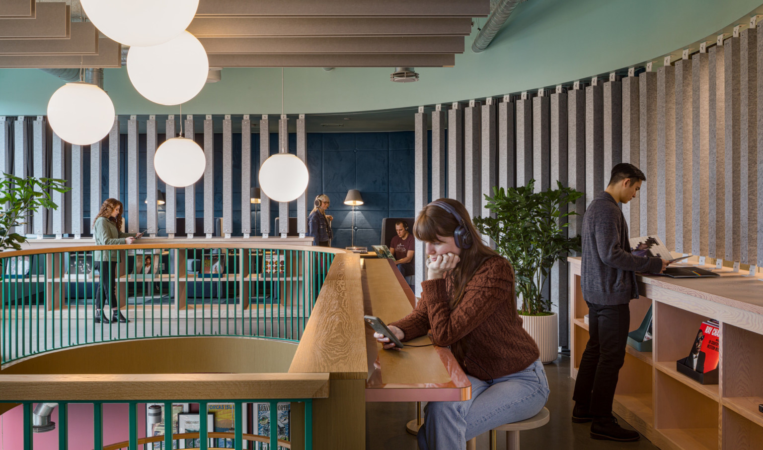 a woman on her phone with headphones sits at a radial wooden counter overlooking a mezzanine finished in wooden slats