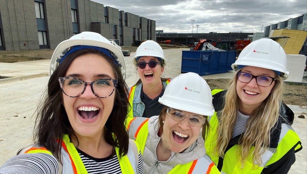 four women in hard hats and reflective vests on a construction site taking a selfie four women in hard hats and reflective vests on a construction site taking a selfie