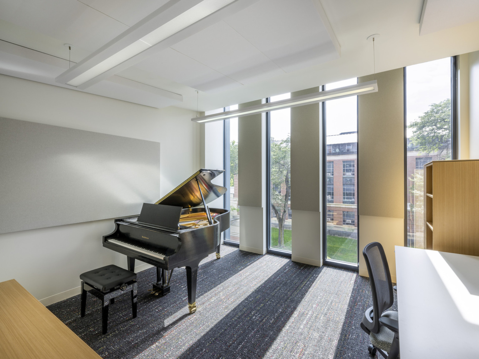 Private piano practice space with desk and panels of floor to ceiling windows on upper floor looking down to courtyard with natural light