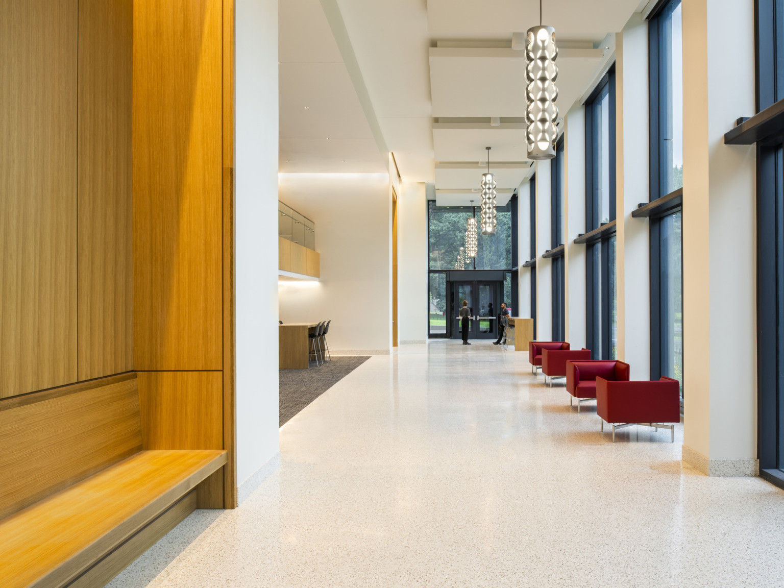 Double height hallway with floor to ceiling windows to courtyard. Wood recessed accent and bench in white hall with mixed seating