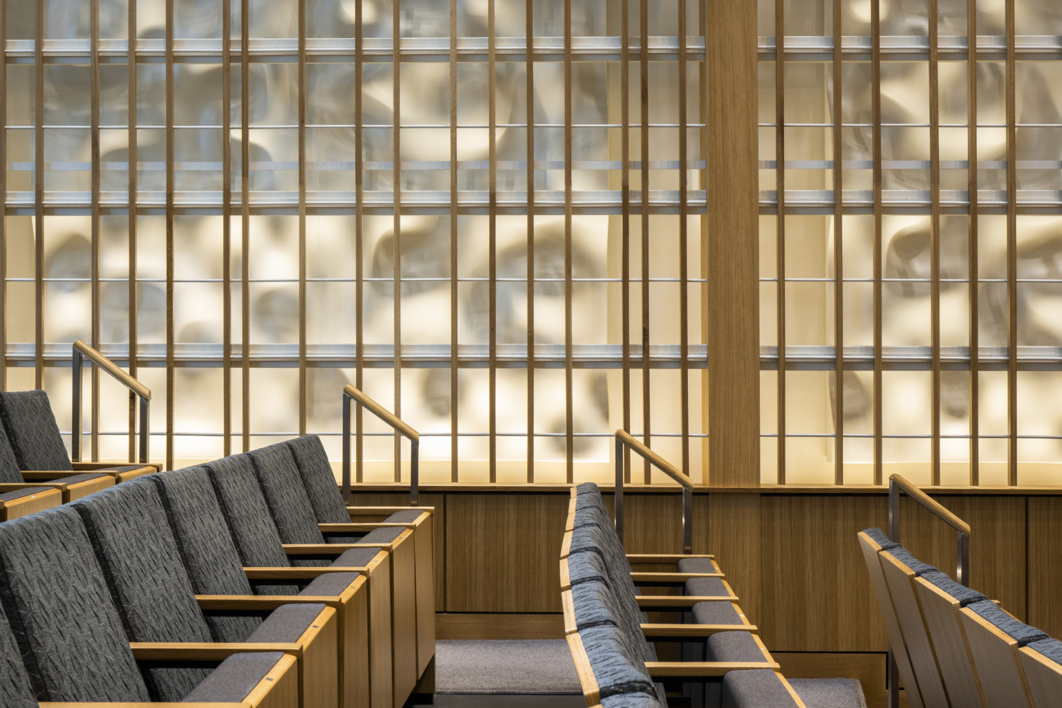 Side view from side of looking down the aisle of grey theater seats with light wood in front of geometric wall panel with organic backlighting