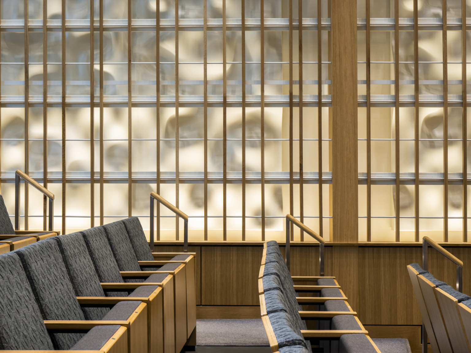 Side view from side of looking down the aisle of grey theater seats with light wood in front of geometric wall panel with organic backlighting