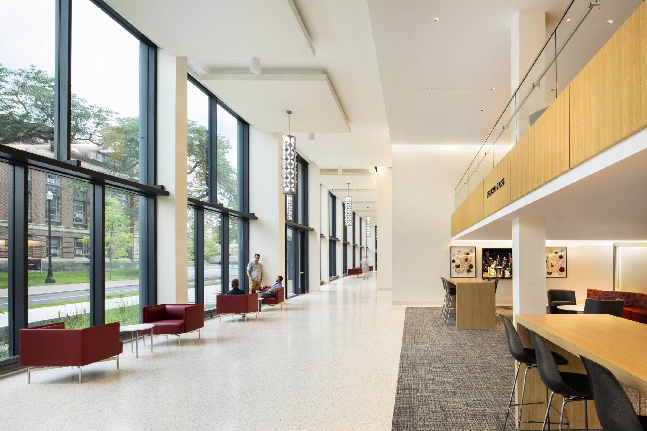 View of double height hallway with floor to ceiling windows to courtyard, left, Music Commons with mixed seating and balcony, right