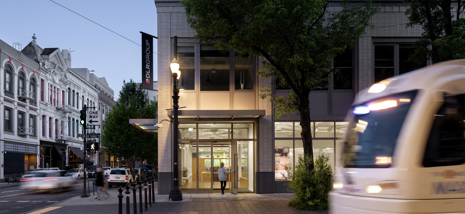 white street car in front of glowing entrance with DLR Group logo banner at the corner of the building in a neighborhood with low rise ornate architecture