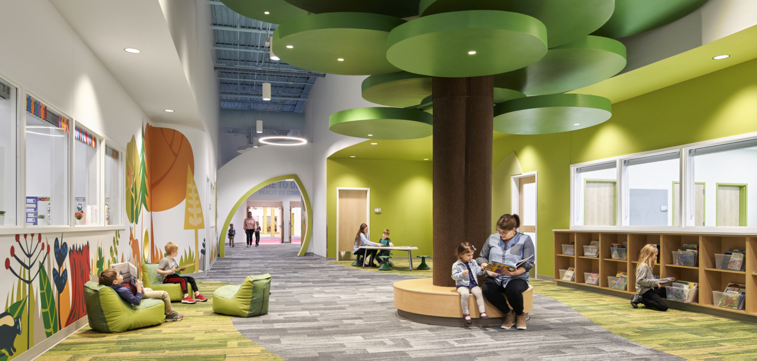 people reading on a brown circular bench with a brown column and green ceiling fixtures in hallway lined with forest graphics