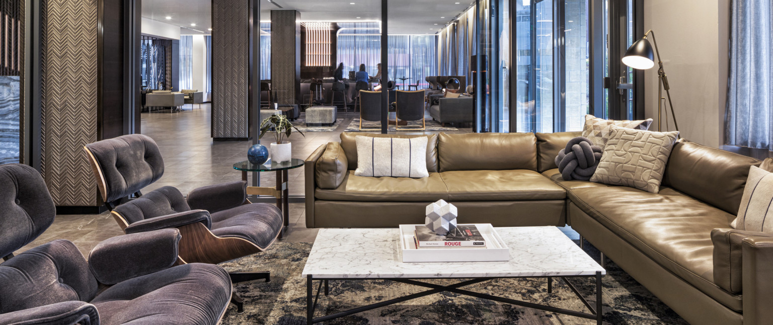 Seating area with couch and arm chairs around coffee table front, sectioned off by glass partition with full length windows