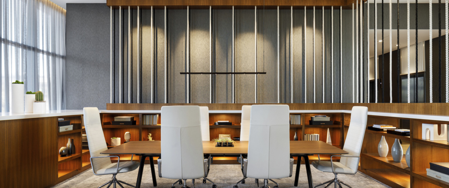 Long wood table with thin white executive chairs in room with wood built in lower shelves with white counter and rope details