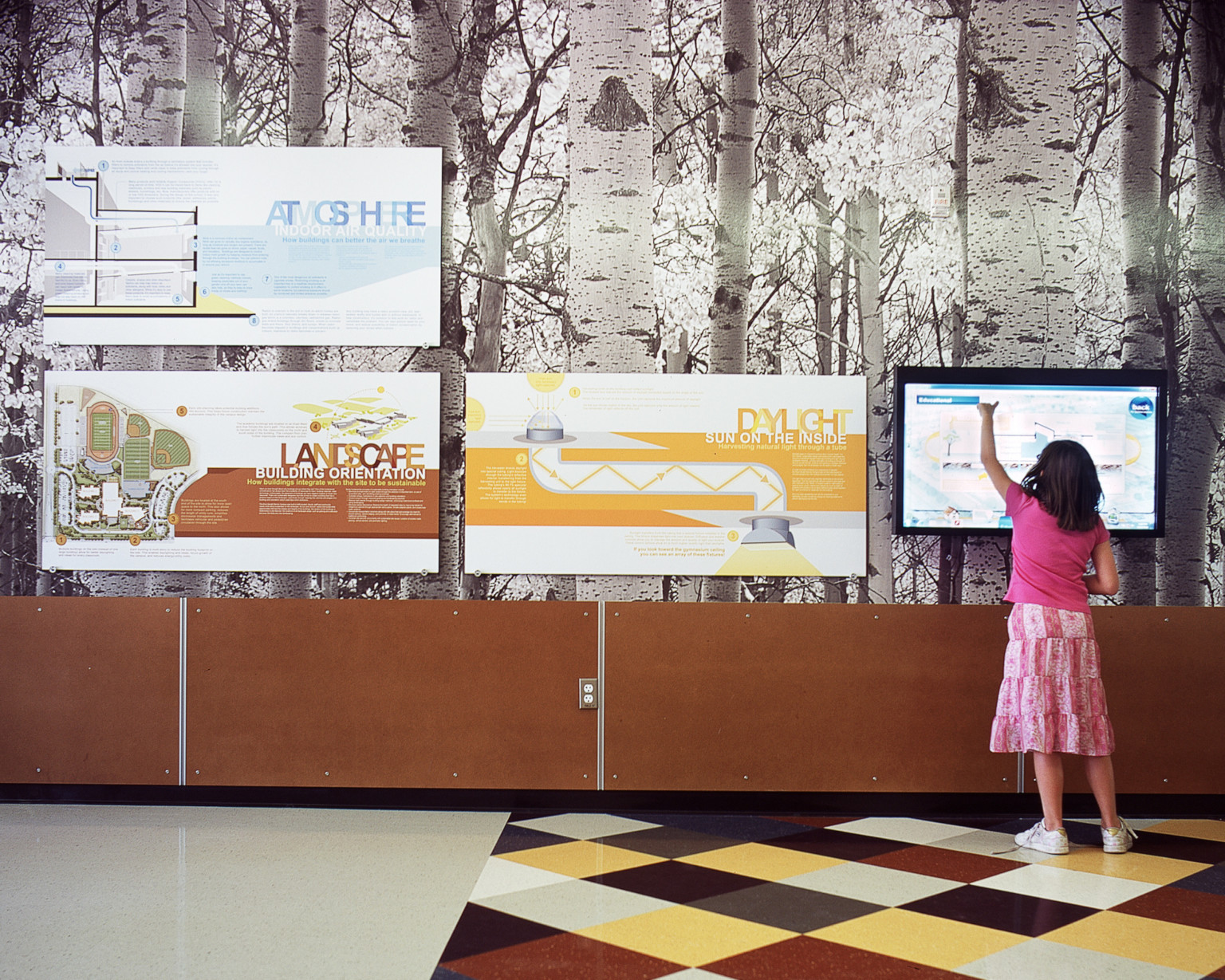 young girl stands at screen on wall with birch tree wallpaper and signage showing the combination of nature with the built environment