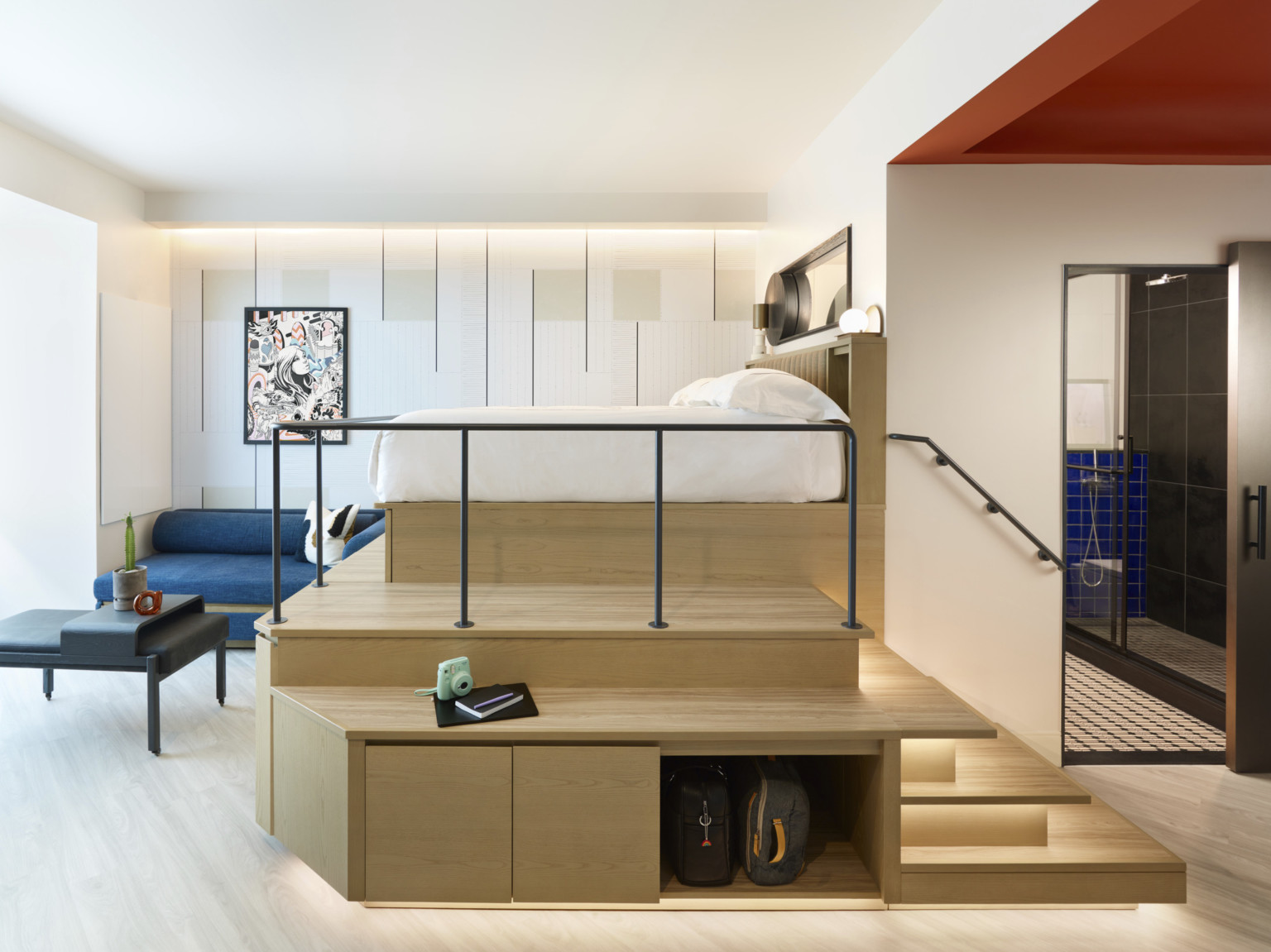 Catbird Hotel guest room with bed on wooden platform on matching wood mezzanine, couch, television and sink on lower level