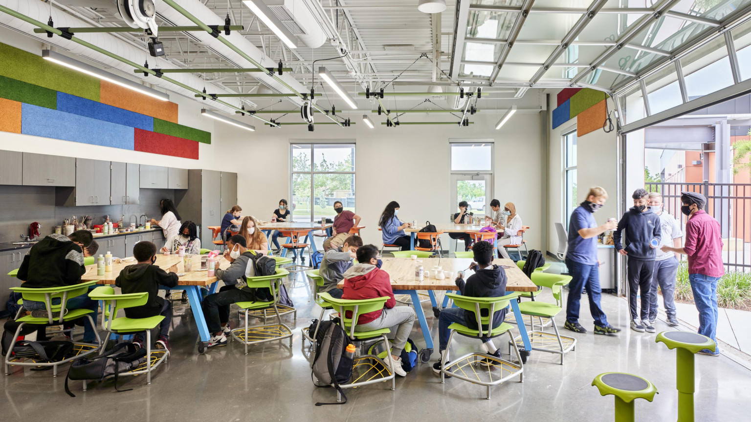 Flexible seating around tables in dining space. Garage door of windows opened to right. Green accents. Kitchenette left