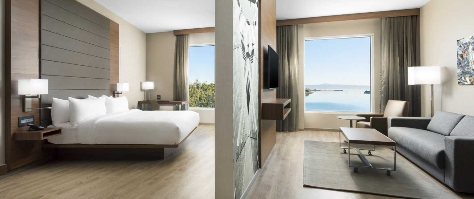 Guest room partially divided from living room by mural and wood panel wall with television. Each room has a large window