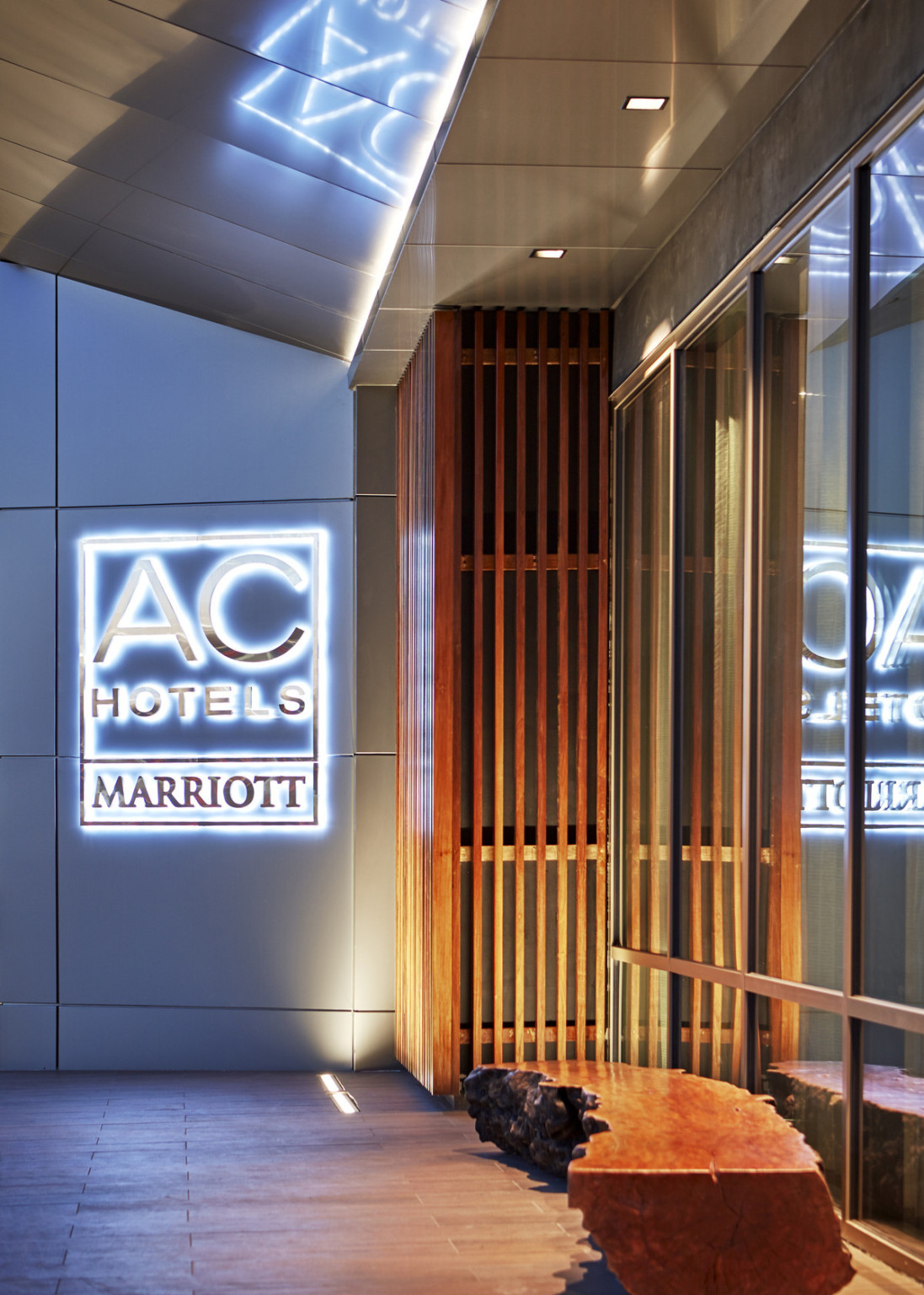 Illuminated signage on white exterior wall reads AC Hotels Marriott, beside wood panel corner detail
