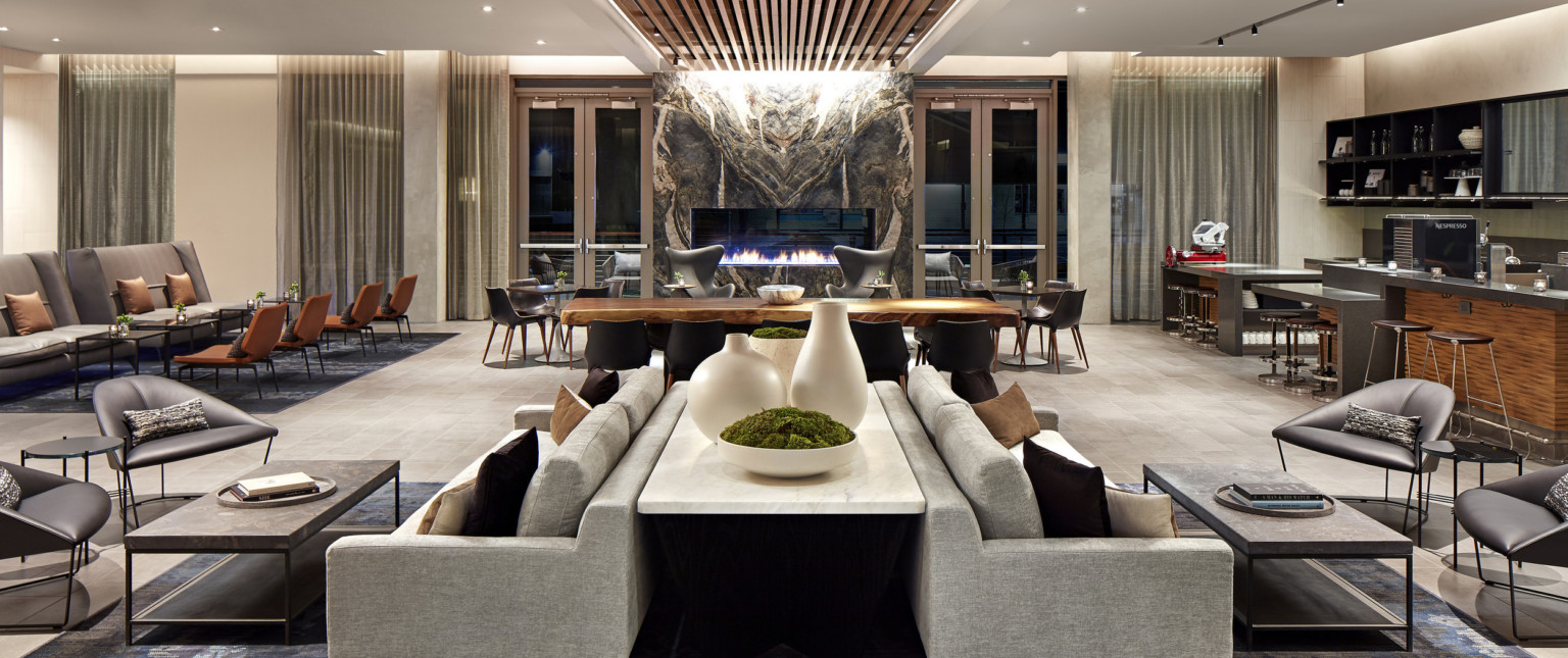 Seating area with couch and tables to the front, wooden table, and armchairs in front of organically carved stone fireplace