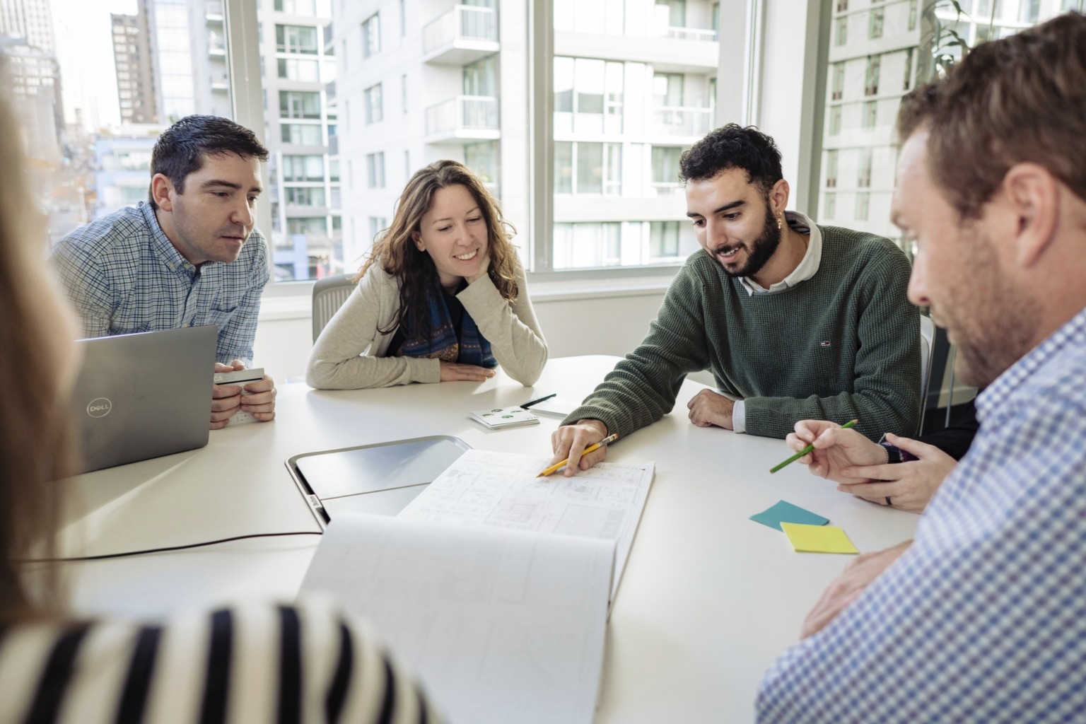 five individuals huddled around a white table with architecture drawings on table, designers collaborating