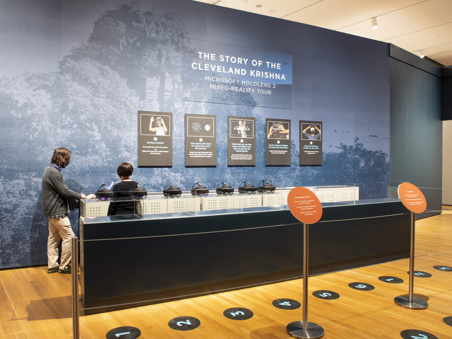 blue tinted wall graphic of cambodian forest with glass display case in the foreground with queueing ropes and tour signs, interactive museum