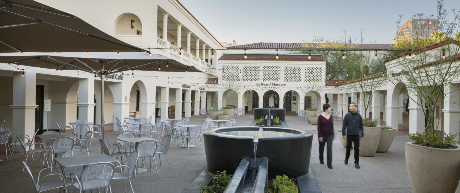 A courtyard with tables and chairs to the left; a fountain runs the central length and lights are strung across the width