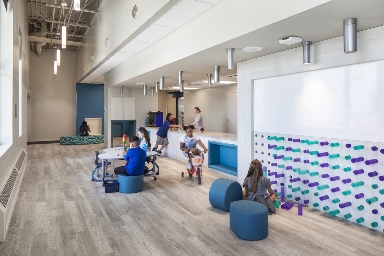 Inside school with interactive wall and white board. Children play in common space in hallway with large windows and counterspace