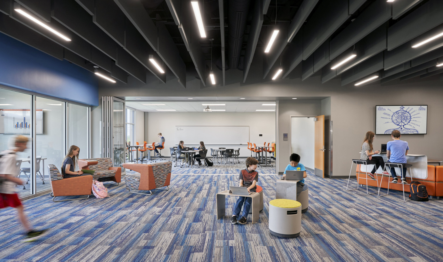 2 rooms with large windows, flexible wall in between. Blue patterned carpet under black ceiling with hanging slats and lights