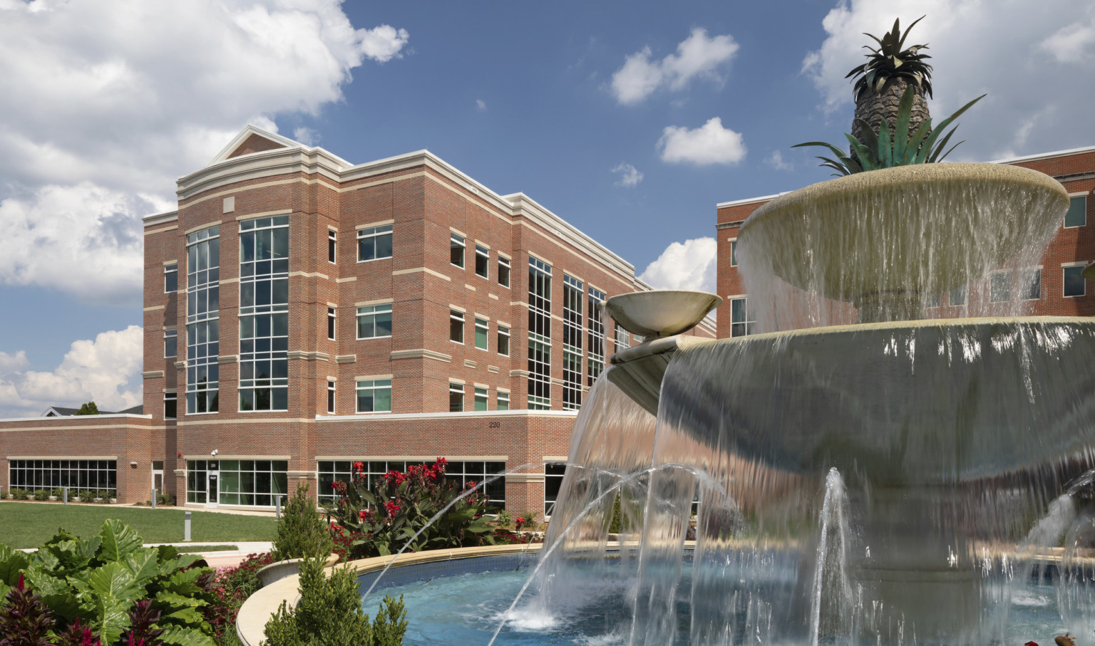 Atrium Health Cabarrus exterior, a brick building with windows along central tower. Landscaped grounds with stepped fountain