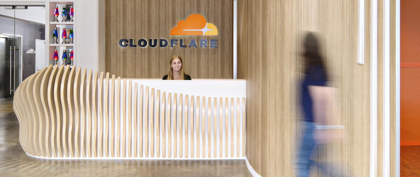 Textural wood panel reception desk in recessed alcove of lobby. Cloudflare logo on wall behind.