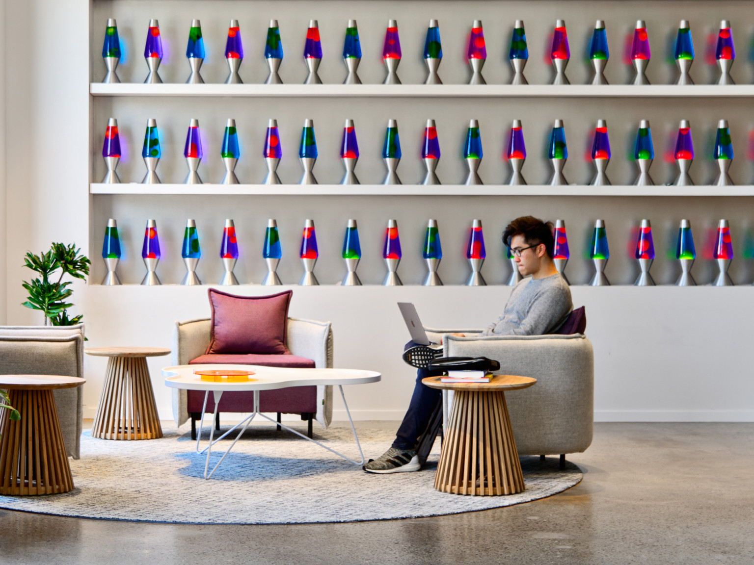 Cloudflare San Francisco Headquarters lobby with mixed comfortable seating and tall ceilings. Wall of blue and pink lava lamps on white built in shelfs