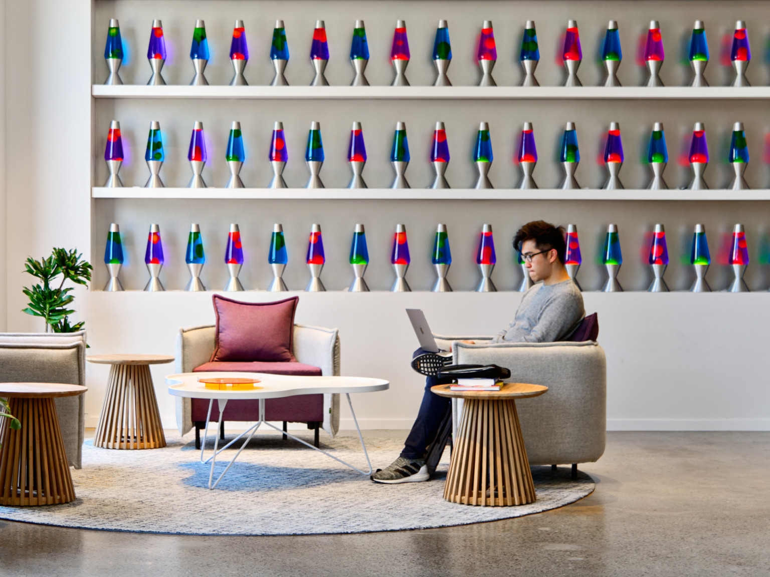 Cloudflare San Francisco Headquarters lobby with mixed comfortable seating and tall ceilings. Wall of blue and pink lava lamps on white built in shelfs