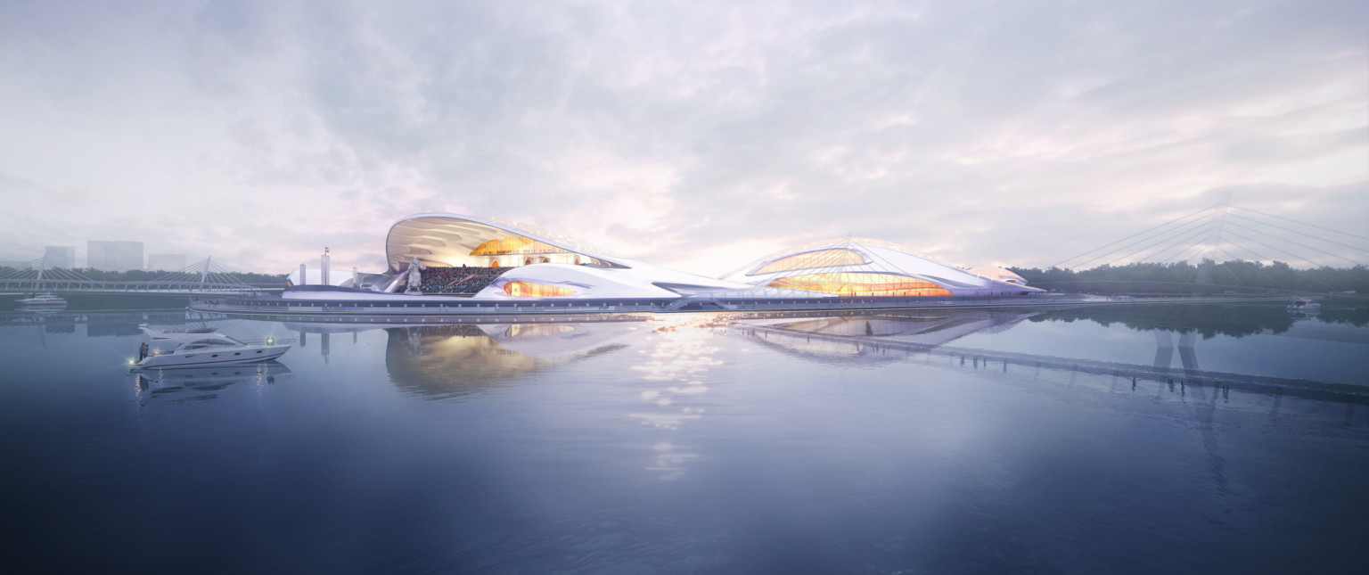 White rounded semicircular building along waterfront with canopied seating area. Complex is illuminated from within