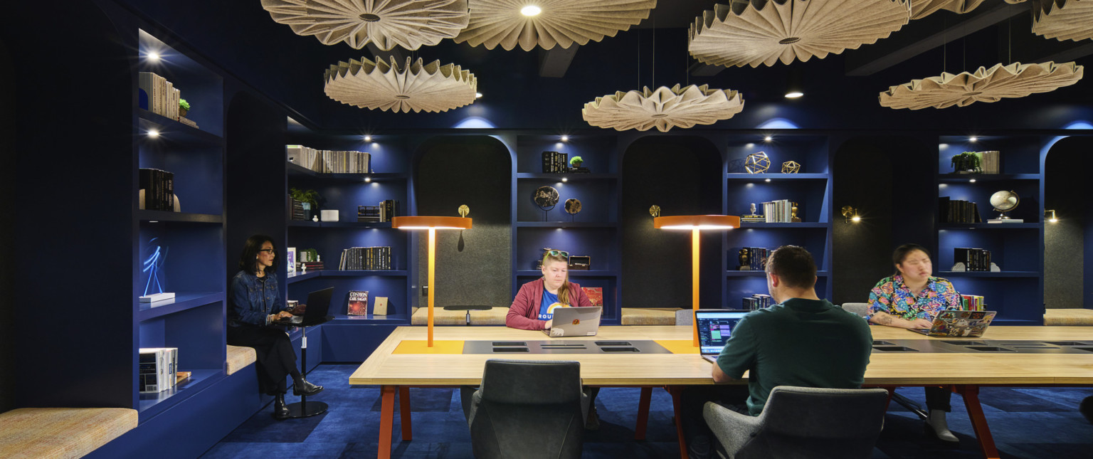 Blue room office common space with long table with built in lights. Sculptural organically shaped illuminated beige accents hang